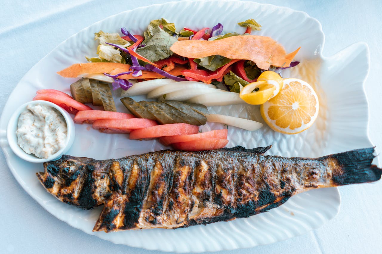 Delicious grilled fish served with fresh vegetables and lemon on a white plate.