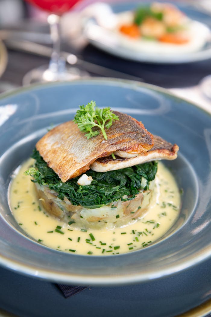 Gourmet fish dish with spinach and cream sauce garnished with herbs.